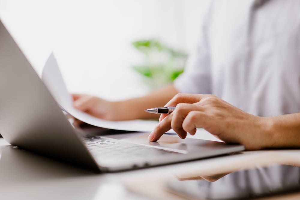online research - a laptop and woman's hands with a pen, taking notes