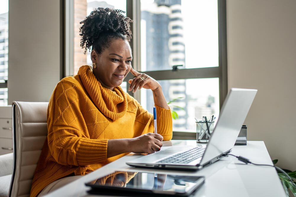 woman studying with a laptop and taking notes by an office window